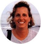 a woman with a beach bag smiles at the camera in front of the ocean